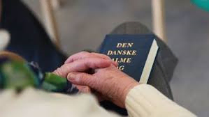 Ældre hænder foldet i skødet over den danske salmebog