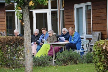 ældre der sidder udenfor og synger med på fællessang