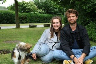 to unge mennesker og en hun sidder på græsset omkring bålet