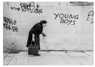 Ældre kvinde med stok mod hvis mur med grafitti