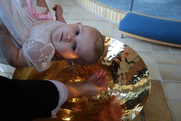 Barn i dåbskjole der holdes over dåbsfad